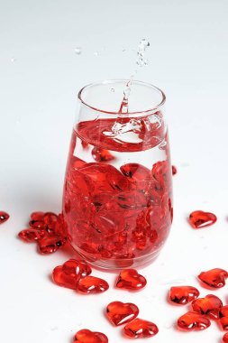 Sevgililer Günü. Bir bardak suda küçük kırmızı cam kalpler. Bir damla sıvı..