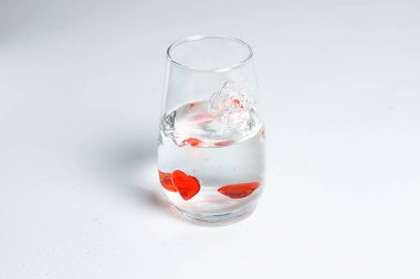 Sevgililer Günü. Bir bardak suda küçük kırmızı cam kalpler. Bir damla sıvı..