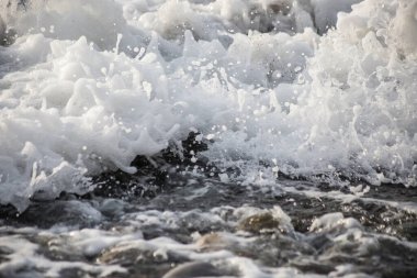 Taşlı ve köpüklü deniz kıyısı, çakıl taşı deniz manzarası. 