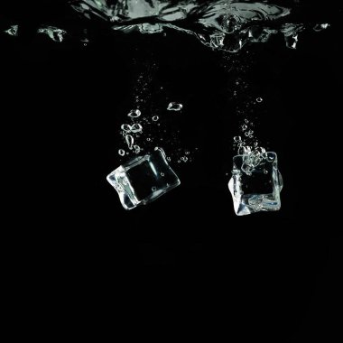 Buz küpleri siyah arka planda suya düşer. Su sıçrıyor ve su altında hava kabarcıkları oluşuyor..