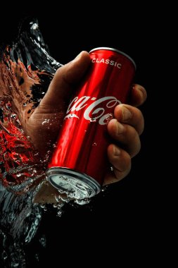 Moskova, Rusya, 7 Nisan 2021. Bir adamın eli bir kutu kola uzatıyor. Su sıçraması ve suyun altında hava kabarcıkları. Siyah arkaplanda izole et.
