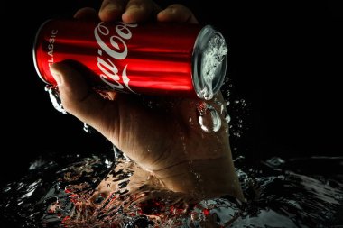 Moskova, Rusya, 7 Nisan 2021. Bir adamın eli bir kutu kola uzatıyor. Su sıçraması ve suyun altında hava kabarcıkları. Siyah arkaplanda izole et.