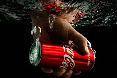 Moskova, Rusya, 7 Nisan 2021. Bir adamın eli bir kutu kola uzatıyor. Su sıçraması ve suyun altında hava kabarcıkları. Siyah arkaplanda izole et.