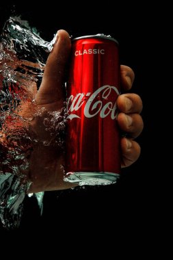 Moskova, Rusya. 6 Nisan 2021. Siyah arka planda kırmızı bir Coca-Cola kutusu. Bir adamın eli bir kutu gazoz uzatıyor. Bir damla su..