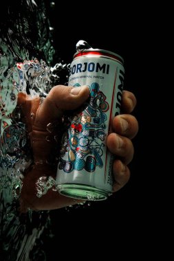 Moskova, Rusya, 7 Nisan 2021. Bir adamın eli bir kutu borjomi uzatıyor. Su sıçraması ve suyun altında hava kabarcıkları. Siyah arkaplanda izole et.