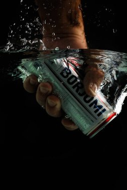 Moskova, Rusya, 7 Nisan 2021. Bir adamın eli bir kutu borjomi uzatıyor. Su sıçraması ve suyun altında hava kabarcıkları. Siyah arkaplanda izole et.