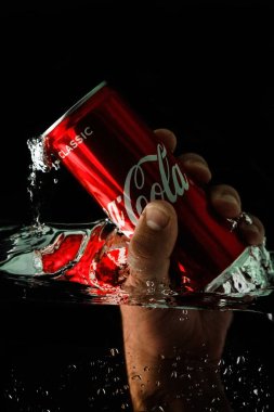 Moskova, Rusya, 7 Nisan 2021. Bir adamın eli bir kutu kola uzatıyor. Su sıçraması ve suyun altında hava kabarcıkları. Siyah arkaplanda izole et.