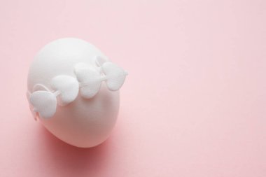 Beyaz kurdeleli bir Paskalya yumurtası. Pembe arka planda kalp şeklinde ve fotokopi alanı var. Mutlu Paskalyalar. Dünya Yumurta Günü