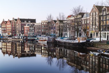 Sabah Amsterdam 'daki Waalseiland Gracht Kanalı' nın manzarası. Bina, tekneler ve yansımalar görülebilir. Metin için boşluk var.