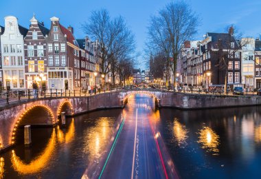 Leidsegracht ve Keizersgracht kanalları kesişme noktalarında Amsterdam'da alacakaranlıkta köprüler görünümü. Bir bot izi görülebilir.