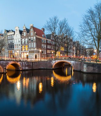 Alacakaranlıkta Amsterdam 'daki Leidsegracht ve Keizersgracht kanallarının kesiştiği köprülerin manzarası. Trafiğin izleri köprüde görülebilir.