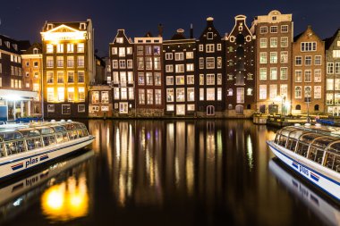 AMSTERDAM, NETHERLANDS - 16 Şubat 2016: Amsterdam 'daki Damrak boyunca eski binalar. Tekneler ve yansımalar görülebilir..
