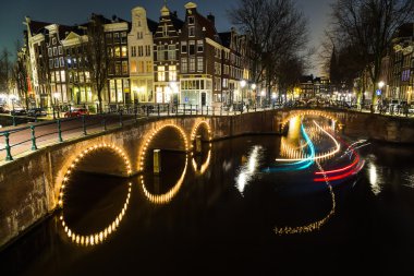 Leidsegracht ve Keizersgracht kanalları kesişme noktalarında Amsterdam'da alacakaranlıkta köprüler görünümü. Bir bot izi görülebilir.