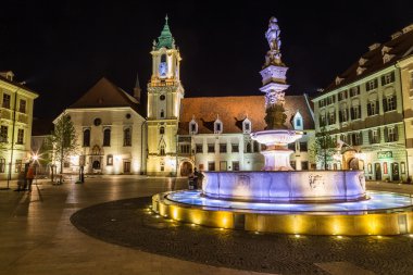 BRATISLAVA, SLOVAKIA - 29 Nisan 2016: Bratislava, Slovakya 'daki Old Town Hall, gece yarısı ön planda Maximilians Çeşmesi ile birlikte. İnsanlar görülebilir..