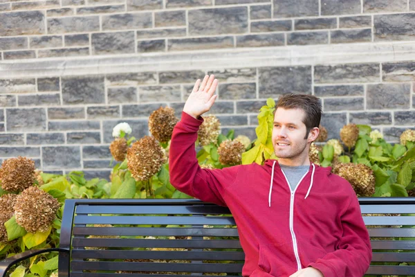 Man waving to somebody from a bench — Stock Photo, Image