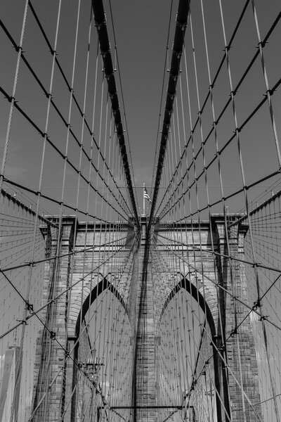 A view of the arches of Brooklyn Bridge in NYC with the bridge, sky and city in black and white