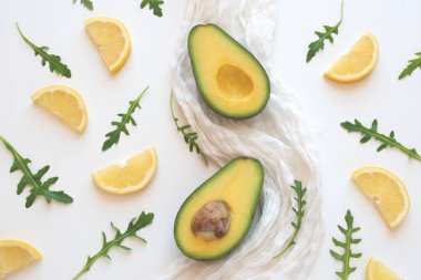 Beyaz peçeteye iki dilim avokado, roka yaprakları ve beyaz arka planda taze limon dilimleri. Üst görünüm.