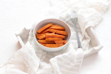 Beyaz tepside bir kasede fırında patates ve beyaz bir peçete.