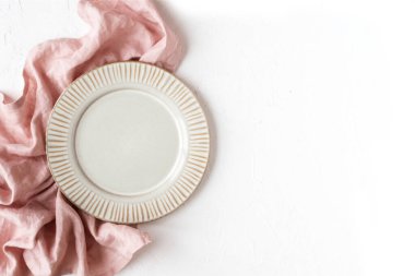 Pembe peçeteli boş bir tabak ve beyaz desenli arka plan, üst manzara, yazı için yer. Tablo ayarı.