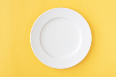 Sarı arka planda yuvarlak beyaz tabak, mutfak aletleri. Düz yat, boşluğu kopyala.