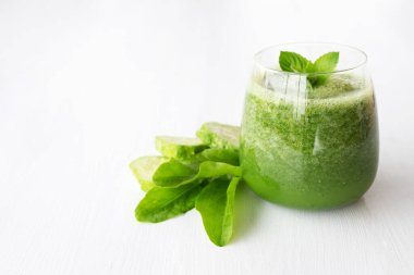 Otlu çiğ yeşil smoothie ve beyaz arka planda salatalık. Detoks, sağlıklı gıda konsepti. Boşluğu kopyala.
