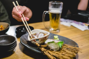 Balık çorbası, sashimi ve birayla birlikte Tokyo restoranında yemek çubuğuyla gezen bir kız.