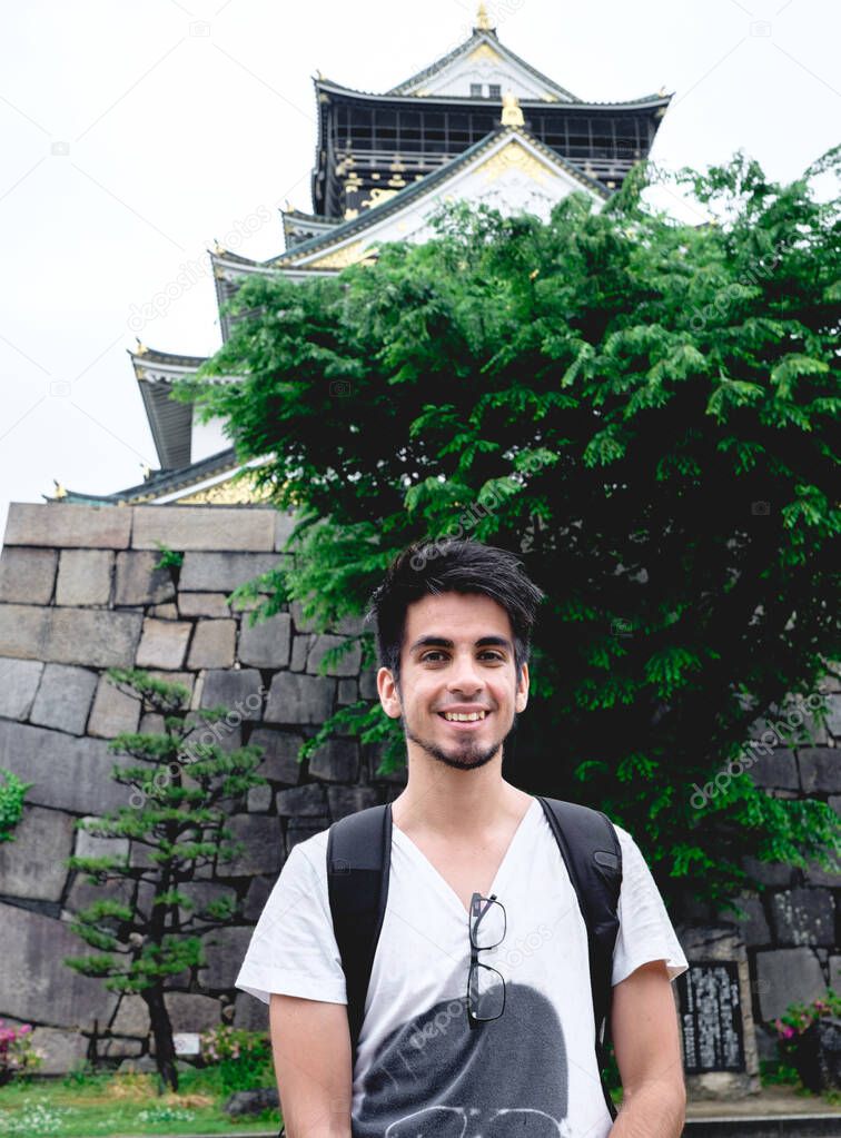 Happy young caucasian traveler with white t-shirt in front of Osaka Castle, Osaka, Japan