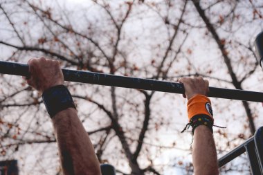 Güneşli bir yaz gününde, spor salonunda barfiks çeken bir sporcunun elleri.