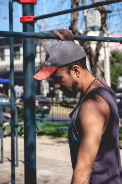 Formda ve yakışıklı bir sporcu güneşli bir yaz gününde sokak antrenman parkında parmaklıklarla esneme hareketleri yapıyor.