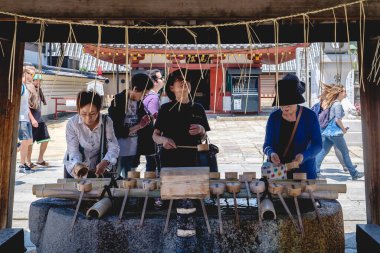Osaka, Japonya - Yaşlı kadınlar ve ziyaretçiler Shitennoji Budist tapınağının girişinde ellerini suyla temizliyorlar 