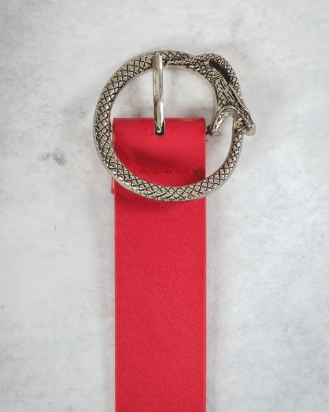 Beautiful red leather belt with silver metal buckle in the shape of snake eating itself (ouroboros) over a smoky gray background