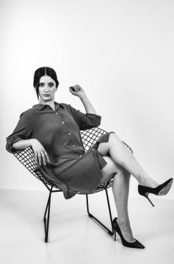 Açık gri stüdyo arka planında stil kıyafetiyle gülümseyen güzel esmer bir kadının moda siyah beyaz portresi.