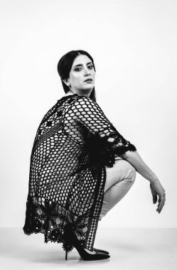 Açık gri stüdyo arka planında stil kıyafetiyle gülümseyen güzel esmer bir kadının moda siyah beyaz portresi.