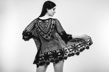 Açık gri stüdyo arka planında stil kıyafetiyle gülümseyen güzel esmer bir kadının moda siyah beyaz portresi.