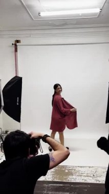 Stüdyo çekiminin sahne arkasında esmer model fotoğrafçı ve stilist için poz veriyor.