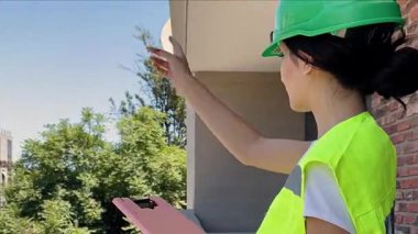 Güvenli yeşil kask ve yansıtıcı yelek giyen profesyonel bir kadın inşaat alanındaki balkondan talimat veriyor.