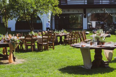 Doğada ziyafet masaları. Düğün bahçede olacak. Açık hava düğünü. Açık büfe. Düğün ziyafeti. Kutlama masası servis tabakları yeşil çimlerin üzerinde duruyor. masa kompozisyonları, bardaklar, mumlar ve tabaklar masaya konur.