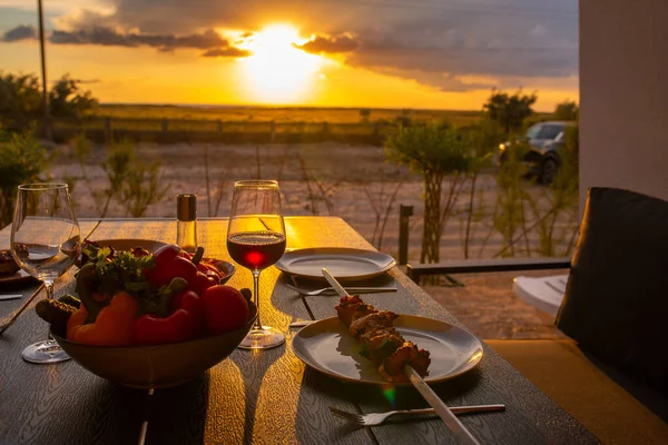 Laid table with food on the summer terrace. Food on the terrace at sunset. Sunset with a laid table for friends. Dinner at home with friends during sunset. Family friendly dinner at home. Dinner terrace for the family. Wine with msom at sunset