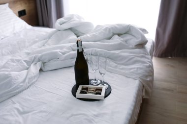 Yatağı geniş yatak odası. Şampanya ve bardaklarla birlikte beyaz çarşaflar. Yaz. Güneş ışınları yatağın üstüne düşer. Sabah yatak odasında şampanya ve şekerlerle. Şampanya ve bardaklı yatak..