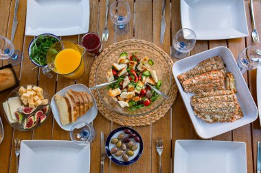 Masanın üstünde akşam yemeği. Akşam yemeğinde salatalı ızgara somon balığı. Terasta büyük bir şirket için akşam yemeği, üst manzara. Masada sağlıklı yemek var. Peynirli ve zeytinli salata. Güzel yemek.