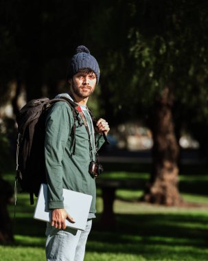 Bilgisayarı, kamerası ve cep telefonu olan dijital göçebe bir sırt çantası. Serbest çalışma projesi üzerinde çalışırken ormanda genç ve yakışıklı bir kadın. Konsept: Seyahat