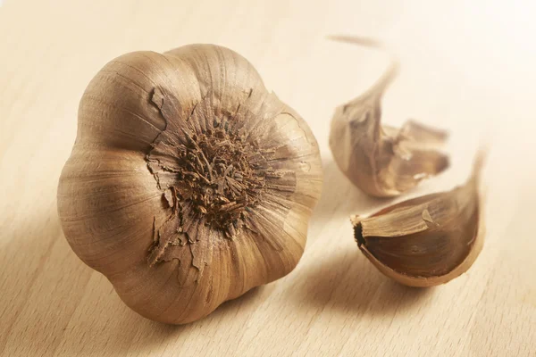 Black or brown garlic on a wooden background with a bright lighting. — Stock Photo, Image