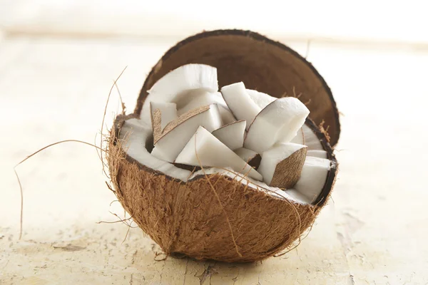 Cocco mezzo pieno di pezzi di cocco su uno sfondo di legno — Foto Stock