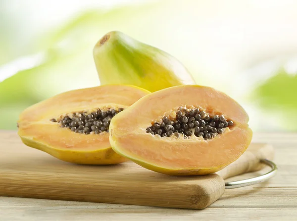 A fa deszkán egész és felére csökkent papaya — Stock Fotó