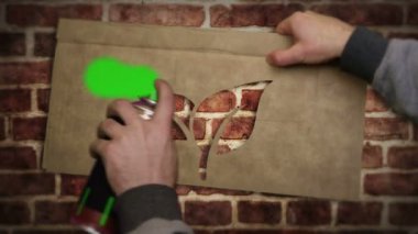 Tuğla duvara eko ikon spreyi boyanmış. Graffiti sanatının çevre dostu ekoloji ve yaprak sembolü. Şehir soyut sanat eserleri. Elinde işaret şablonuyla hava fırçası boyası.