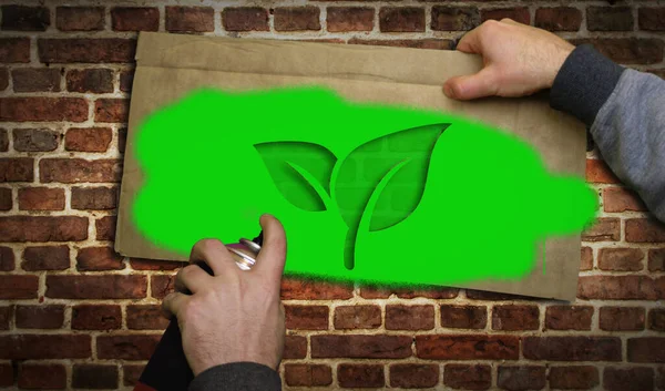 Eco icon spray painted on the brick wall. Graffiti art concept ecology friendly and environment leaf symbol. Urban abstract artwork. Airbrush paint with sign template in hand.