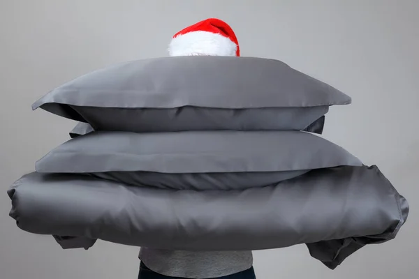 Noel Baba şapkalı kadın sıcak bir yorgan ve gri tüy yastık tutuyor. Uyumak için yatak.