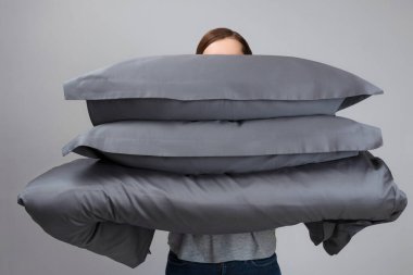 Kadın sıcak bir yorgan ve gri tüy yastık tutuyor. Uyumak için yatak.