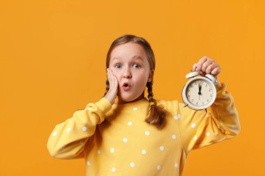 Alarmlı saatle şok olmuş küçük bir kız. Sarı arka plandaki çocuk.