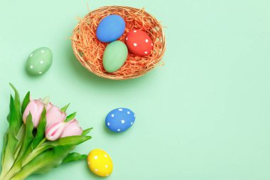Sepette paskalya yumurtaları, yeşil arkaplanda pembe laleler. Düz yatay kopyalama alanı olan üst görünüm.